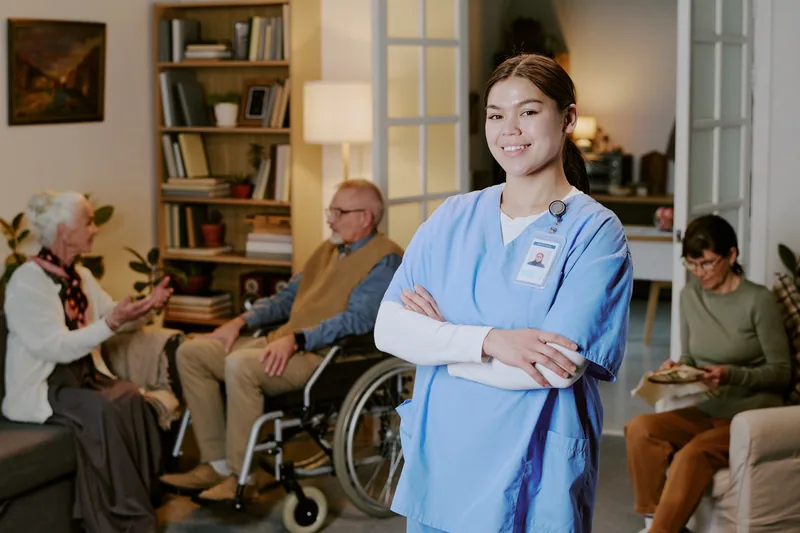 A smiling woman in blue scrubs in a living room with older adults