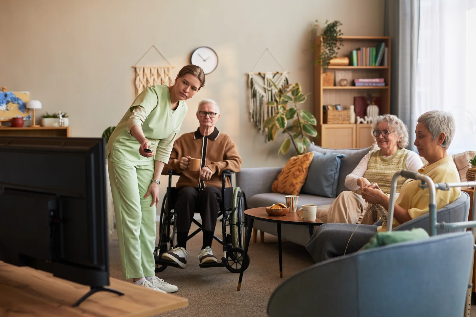 A woman in green scrubs with three older adults in a shared living room