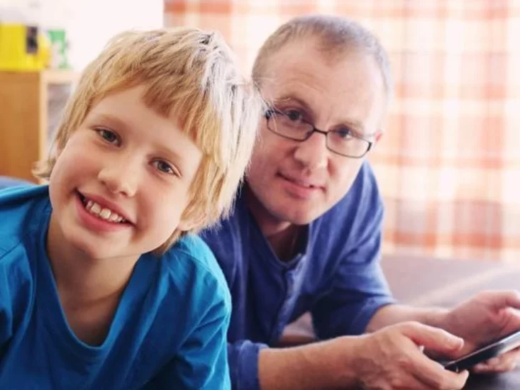 A young kid smiling with a man lying besides him