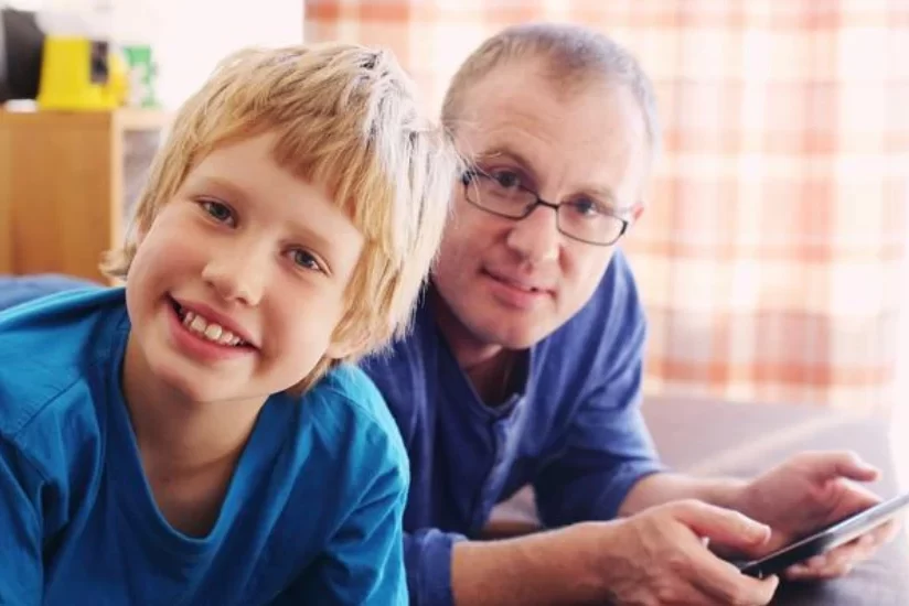 A young kid smiling with a man lying besides him