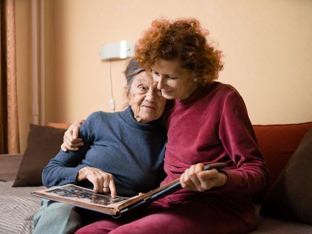A woman showing some photos in an album to a senior old woman