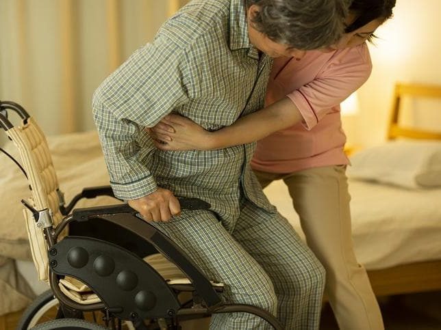 A young homecare provider holding an old patient from a wheelchair
