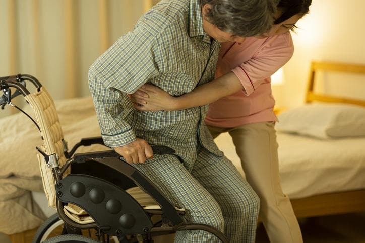 A young homecare provider holding an old patient from a wheelchair