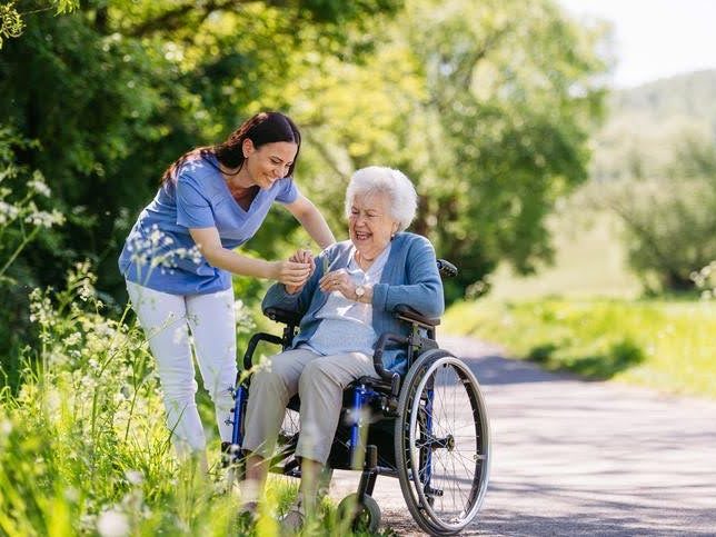 EQC caregiver making an old woman on a wheelchair laugh